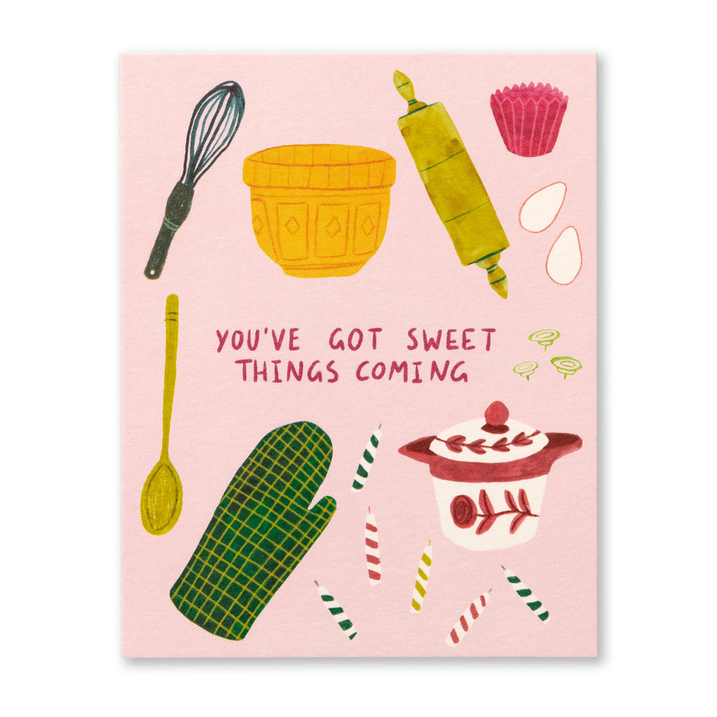 Birthday Greeting Card - You've Got Sweet Things Coming. Illustration shows a pink background with ingredients to make a cake and the baking tools to make it. Some items include an oven mitt, birthday candles, eggs, a whisk, a rolling pin, and cupcake tins.