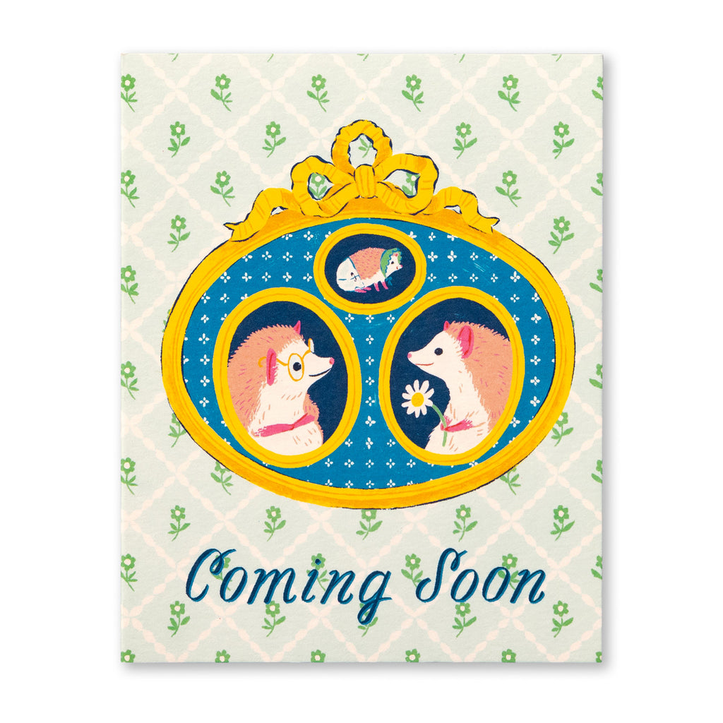 Baby Greeting Card - Coming Soon. Illustration shows two parent hedgehogs and a baby hedgehog in a bonnet in an ornate photo frame. The background looks like ornate wallpaper and has text at the bottom.