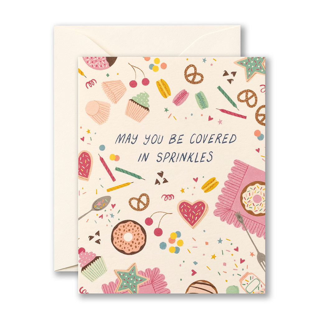 Birthday Greeting Card - May You Be Covered in Sprinkles. Ilustration shows sweet snack foods scattered around, including donuts, cupcakes, cookies, macarons, cherries, and more. There are sprinkles and birthday candles everywhere.
